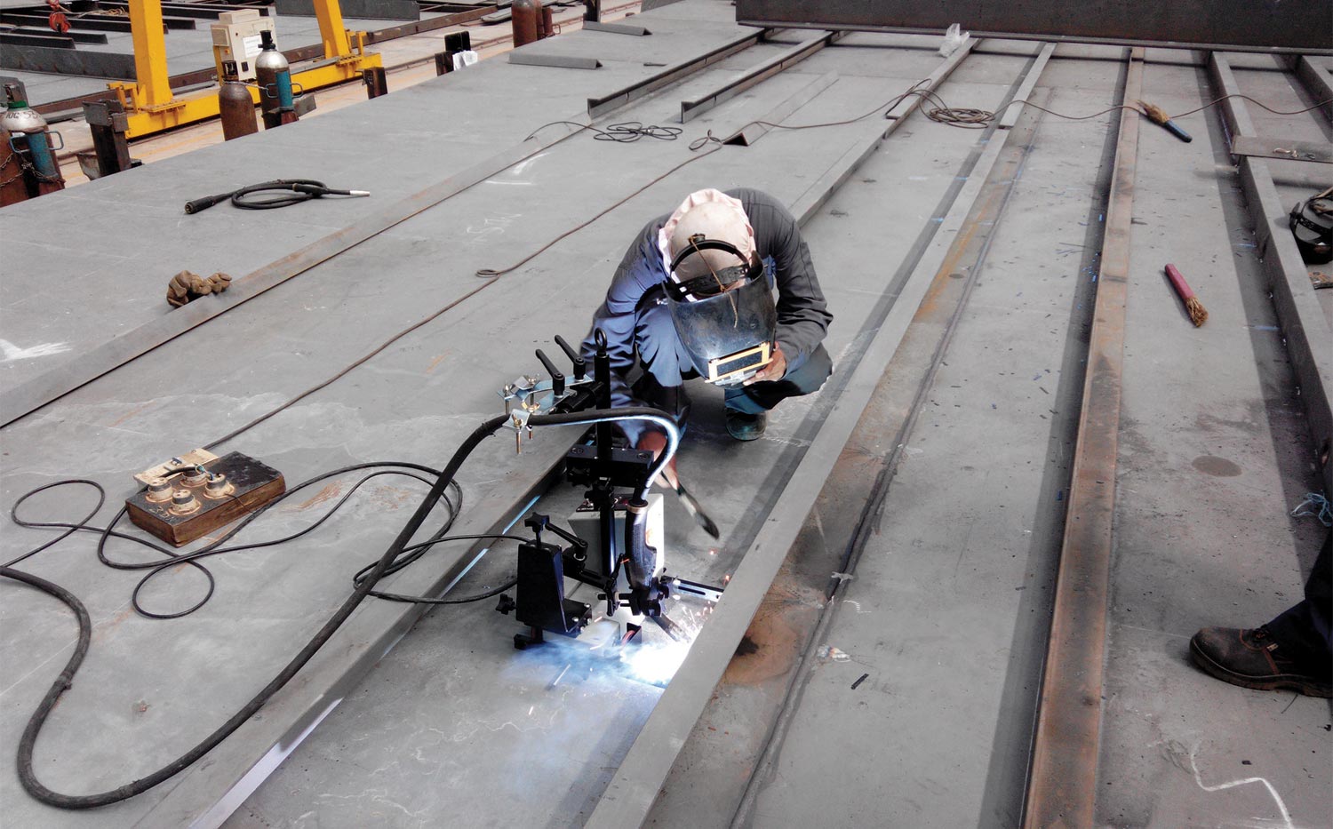 a factory worker supervises a welding robot at work